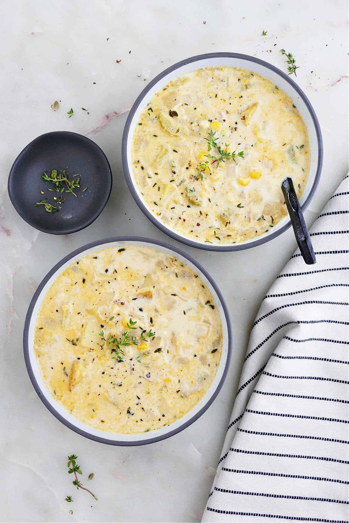 two bowls of sweet corn soup topped with fresh thyme sprigs on a counter