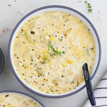 sweet corn soup in a bowl with fresh thyme and a black spoon on a counter