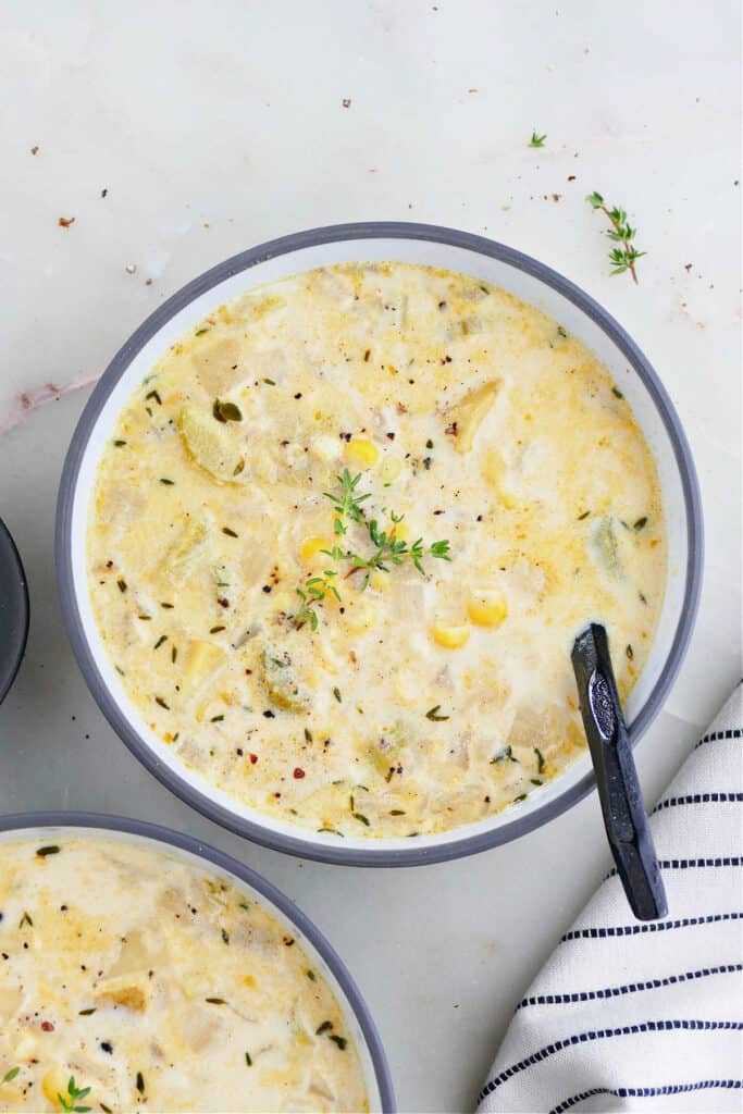 sweet corn soup in a bowl with fresh thyme and a black spoon on a counter