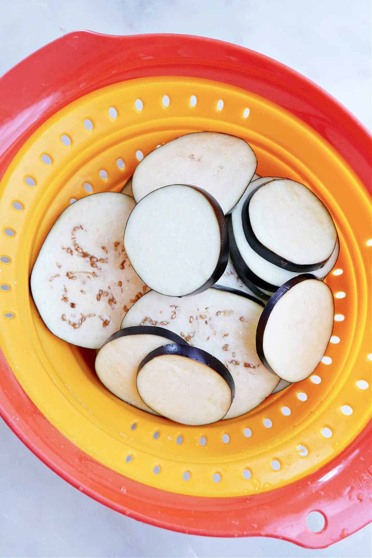 sliced eggplant rounds sprinkled with salt and sweating in a colander