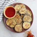 crispy baked eggplant slices on a serving dish with marinara sauce next to a striped napkin