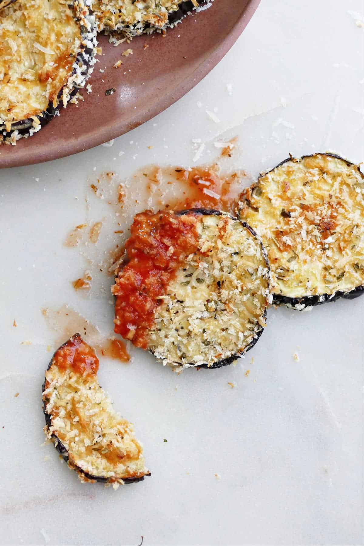 three crispy baked eggplant slices dipped in marinara on a marble counter