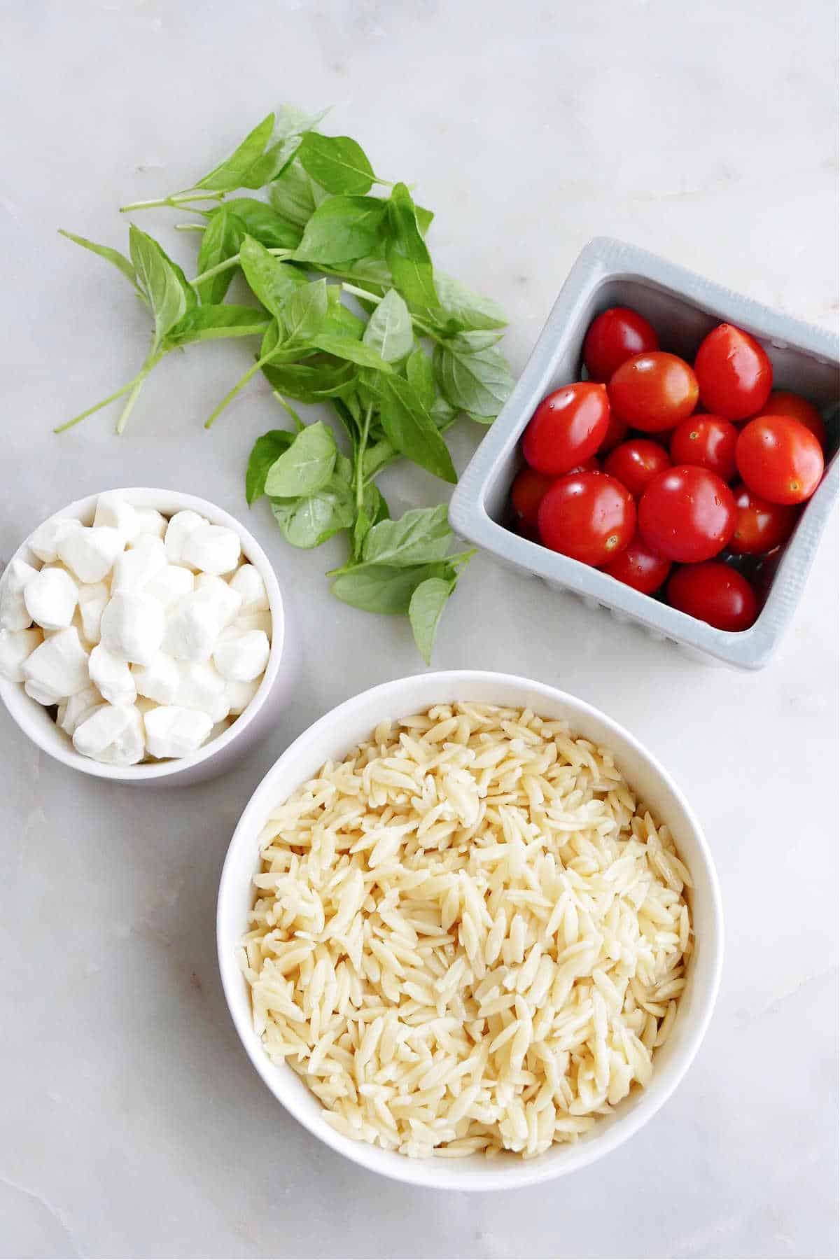 orzo pasta, mozzarella pearls, cherry tomatoes, and basil leaves on a counter