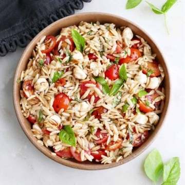 caprese orzo salad in a serving dish next to basil and a napkin