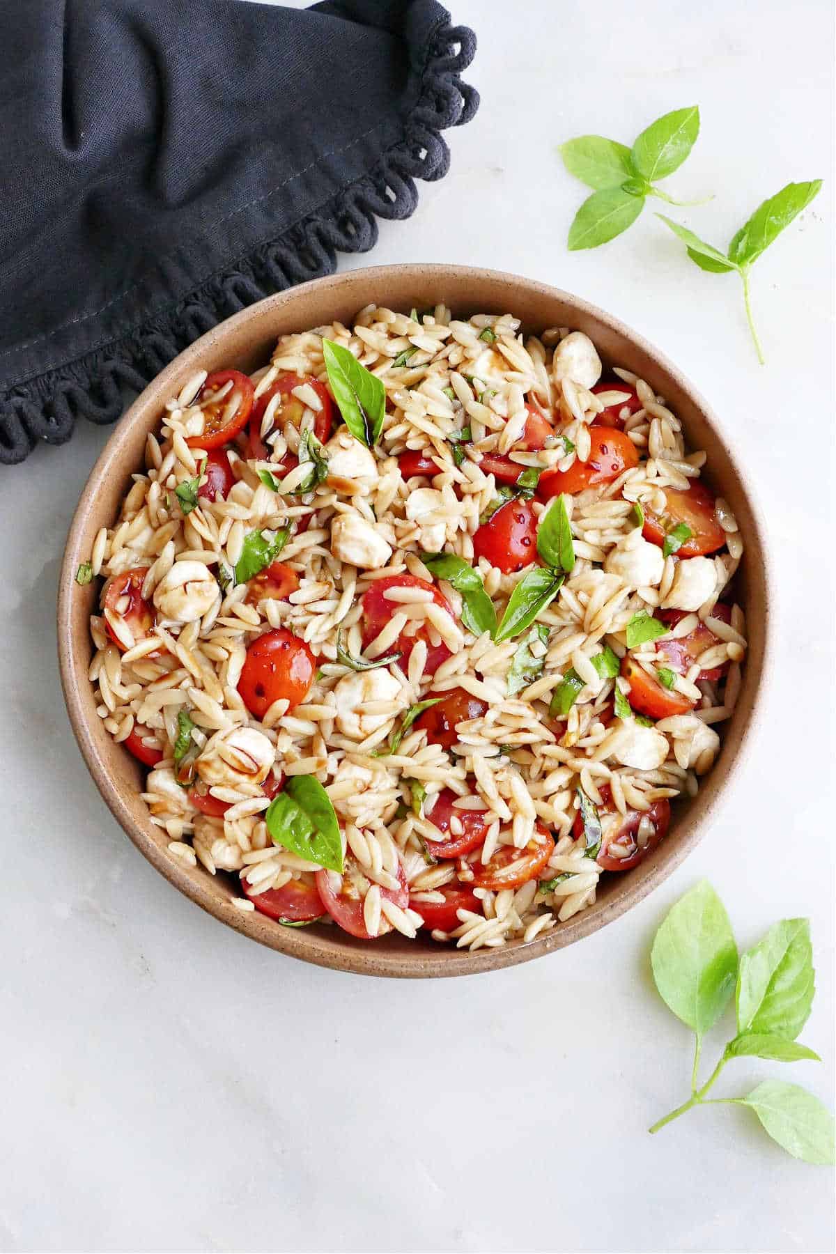 caprese orzo salad in a serving dish next to basil and a napkin