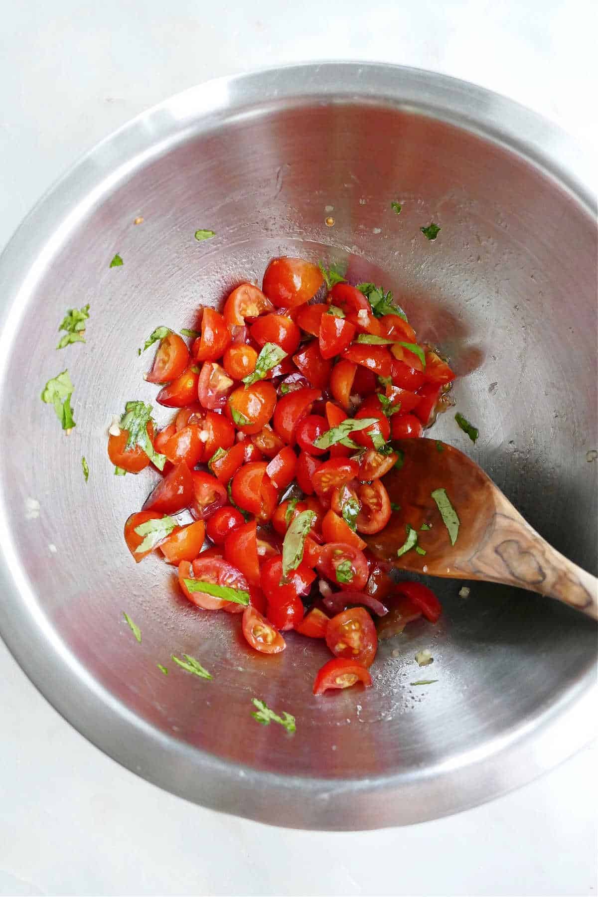 cherry tomato bruschetta being mixed together with a wooden spoon in a bowl