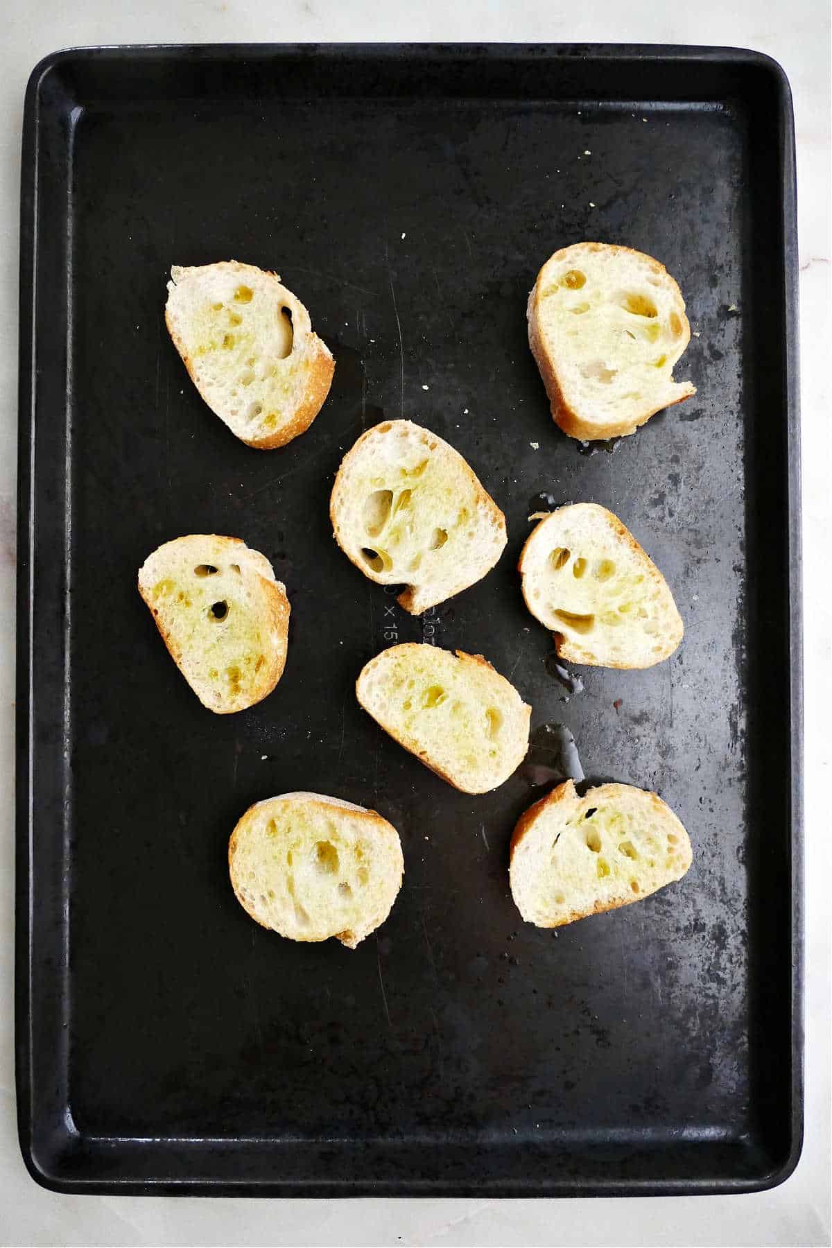 seven slices of baguette brushed with olive oil on a baking sheet