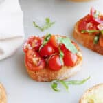 cherry tomato bruschetta topped with fresh basil on a counter next to ingredients