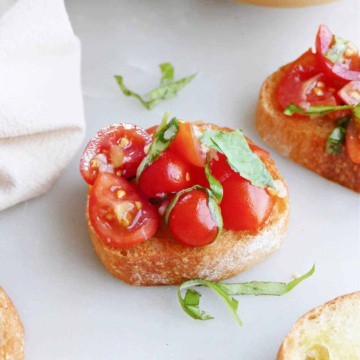 cherry tomato bruschetta topped with fresh basil on a counter next to ingredients