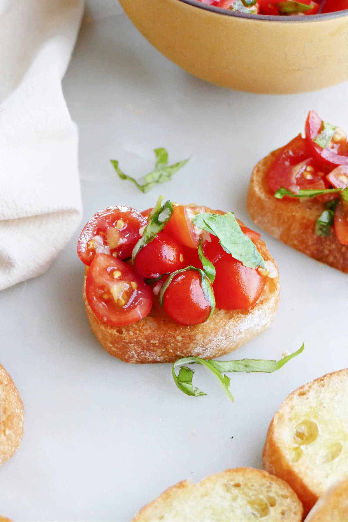 cherry tomato bruschetta topped with fresh basil on a counter next to ingredients