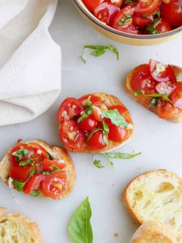 three cherry tomato bruschetta slices next to plain bread slices and topping