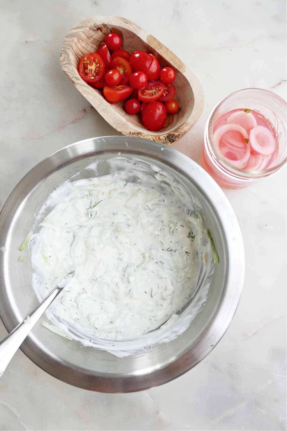 tzatziki sauce, tomatoes, and red onions on a counter next to each other