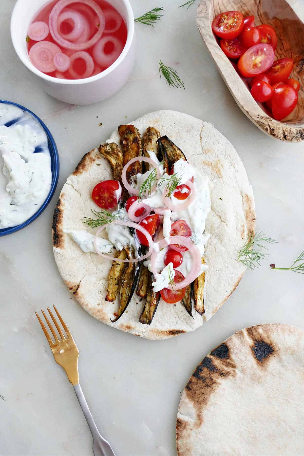 roasted eggplant slices and gyro toppings on a pita next to other ingredients