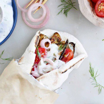 eggplant gyro sandwich on pita wrapped up in foil and parchment paper next to toppings