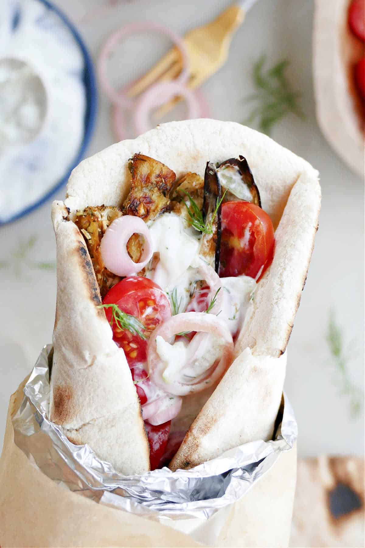 woman holding an eggplant gyro sandwich wrapped in foil and paper over a counter