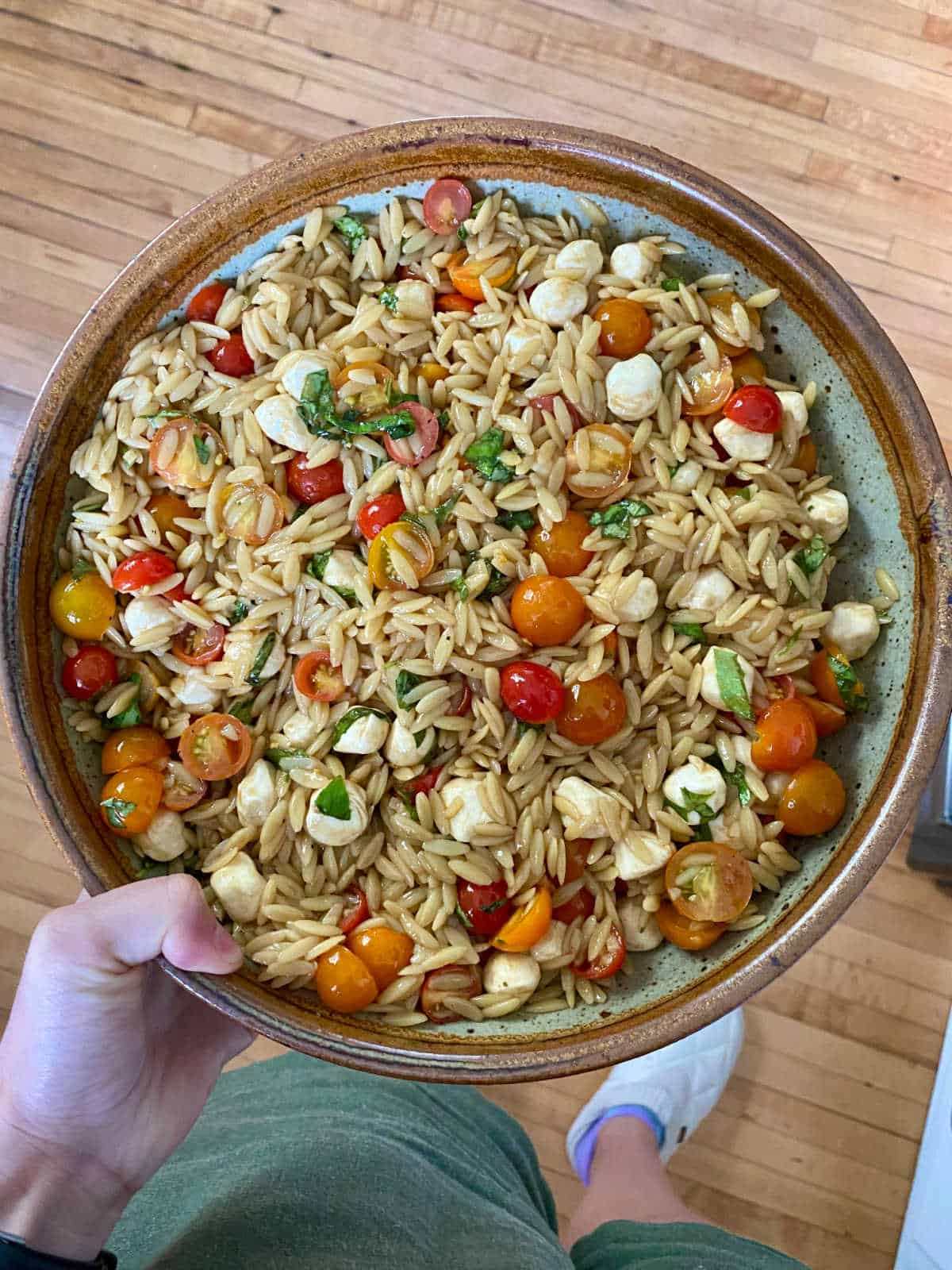 caprese orzo salad in a salad bowl that a woman is holding