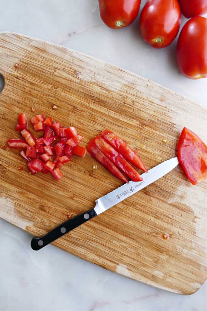 cubed and sliced roma tomatoes on a cutting board with a serrated knife