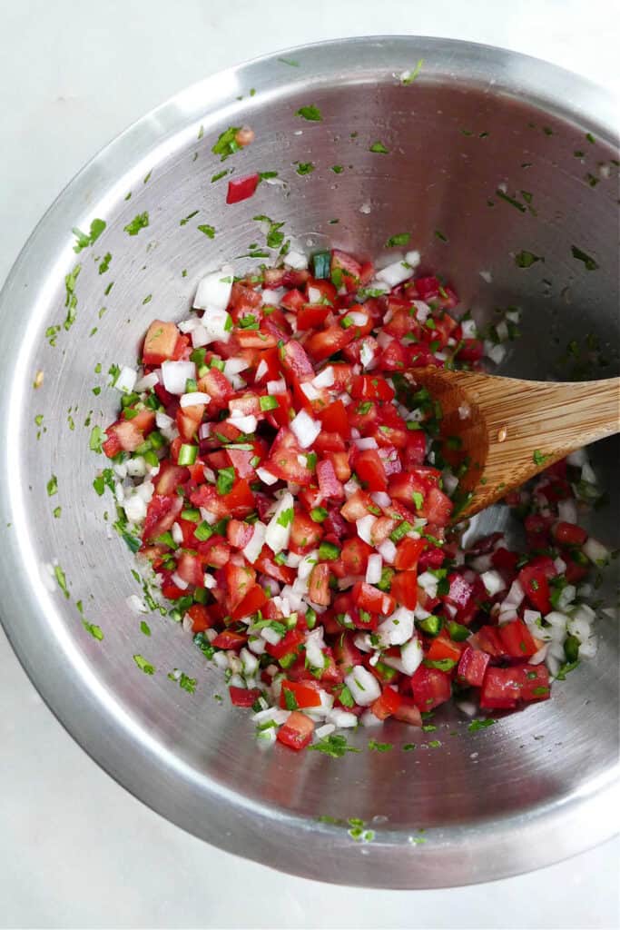 ingredients for garden salsa being mixed together with a spoon in a bowl