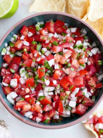 fresh garden salsa in a serving bowl surrounded by tortilla chips and ingredients
