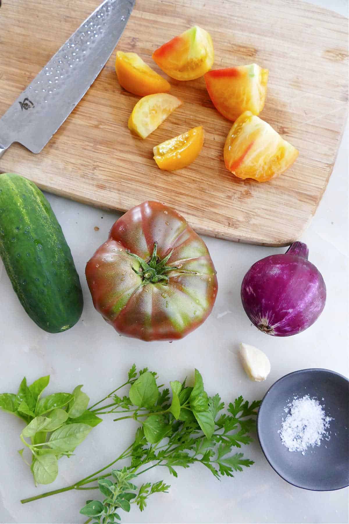 cutting board and knife with chopped tomatoes and other ingredients for the salad next to it