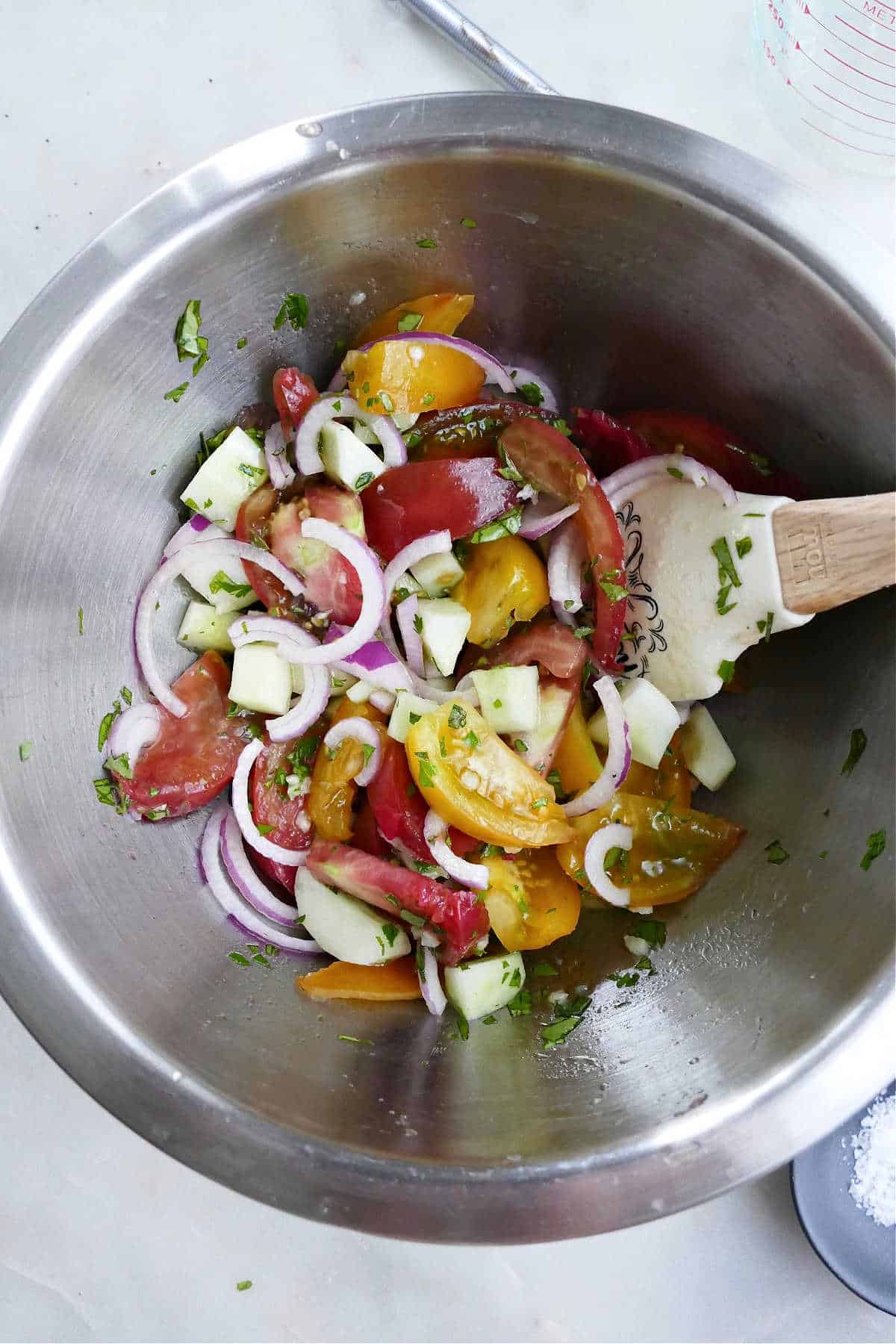 sliced tomatoes, cucumbers, and red onion in a mixing bowl with a spatula