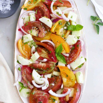 heirloom tomato and cucumber salad topped with fresh herbs on a serving platter