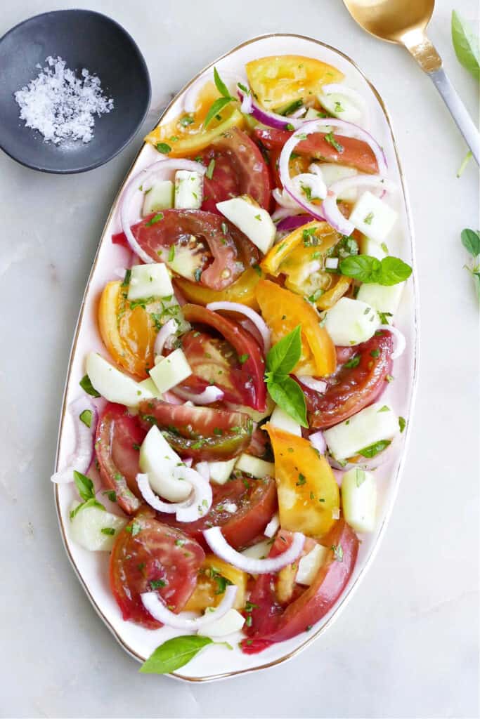 heirloom tomato salad with onion and cucumber on an oval serving platter on a counter
