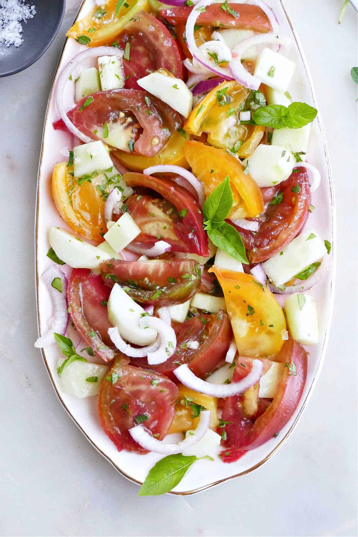 tomato, cucumber, and onion salad with herbs on a serving platter on a counter