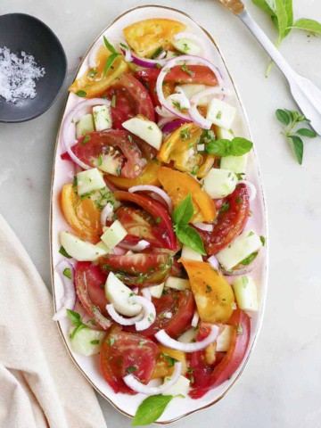 heirloom tomato and cucumber salad topped with fresh herbs on a serving platter