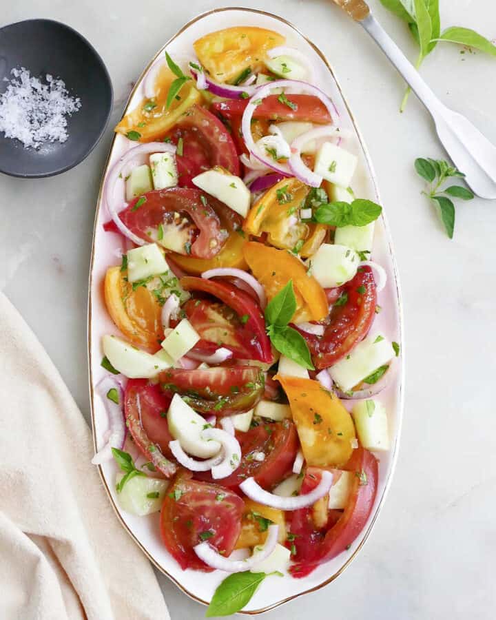 heirloom tomato and cucumber salad topped with fresh herbs on a serving platter