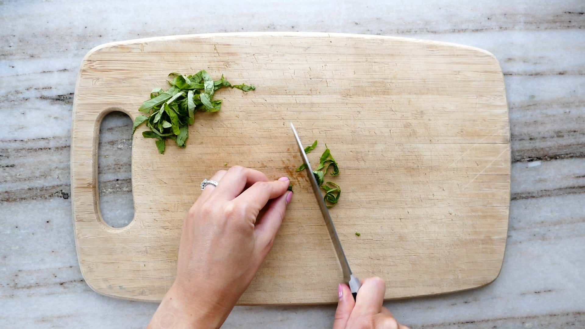 woman slicing basil into chiffonade on a bamboo cutting board