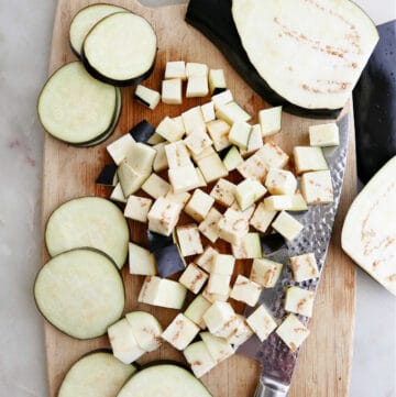diced and sliced eggplant spread out on a bamboo cutting board next to a knife