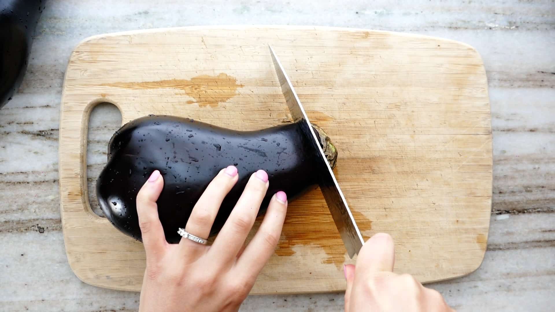 woman trimming off the stem of an eggplant over a bamboo cutting board