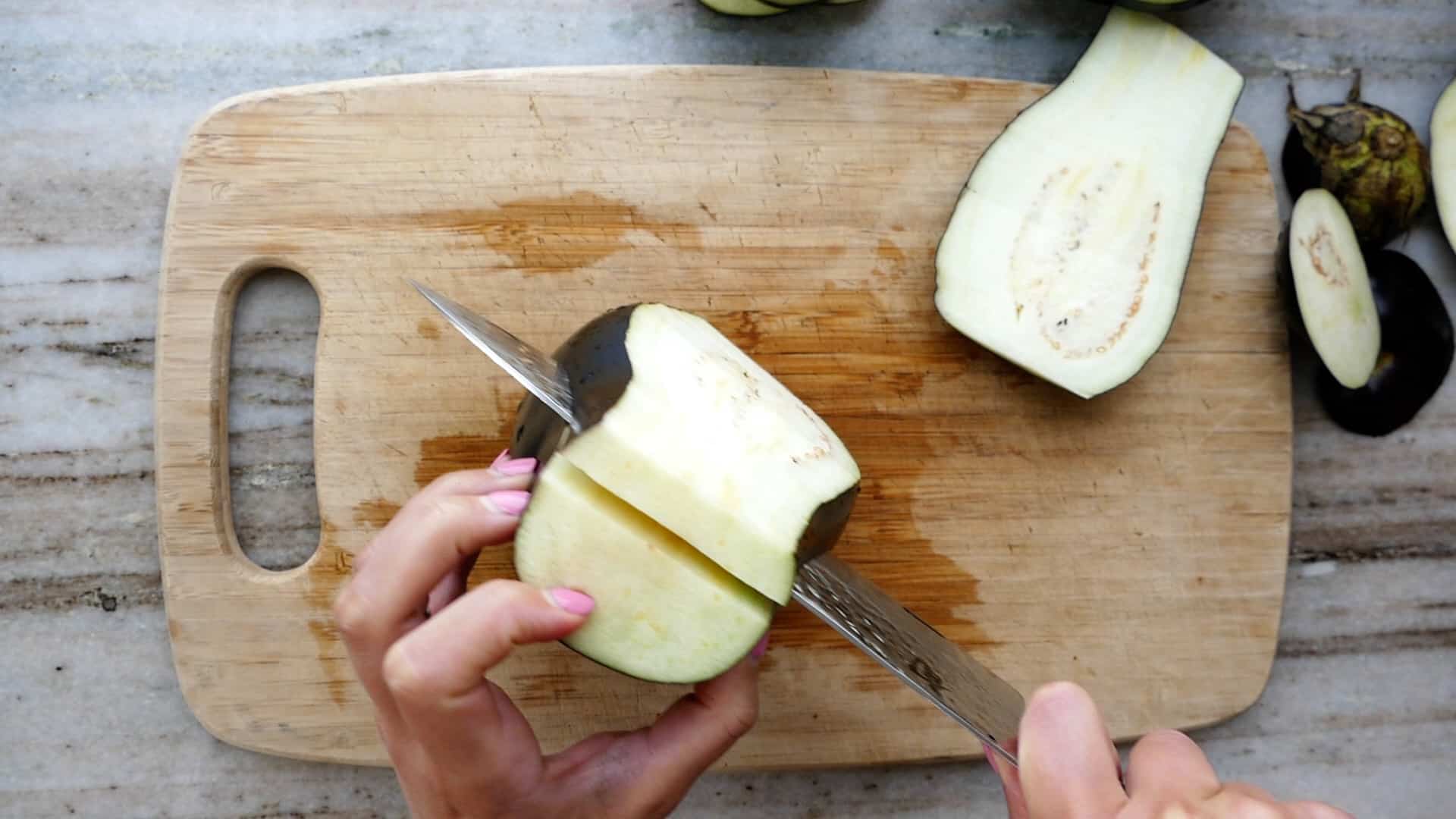 woman cutting an eggplant into slabs over a bamboo cutting board