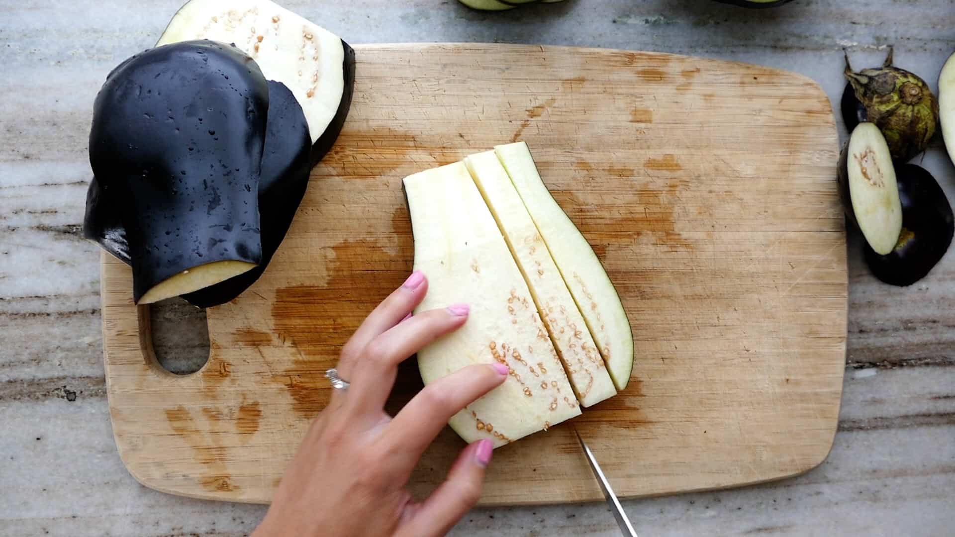 woman cutting an eggplant into strips over a bamboo cutting board