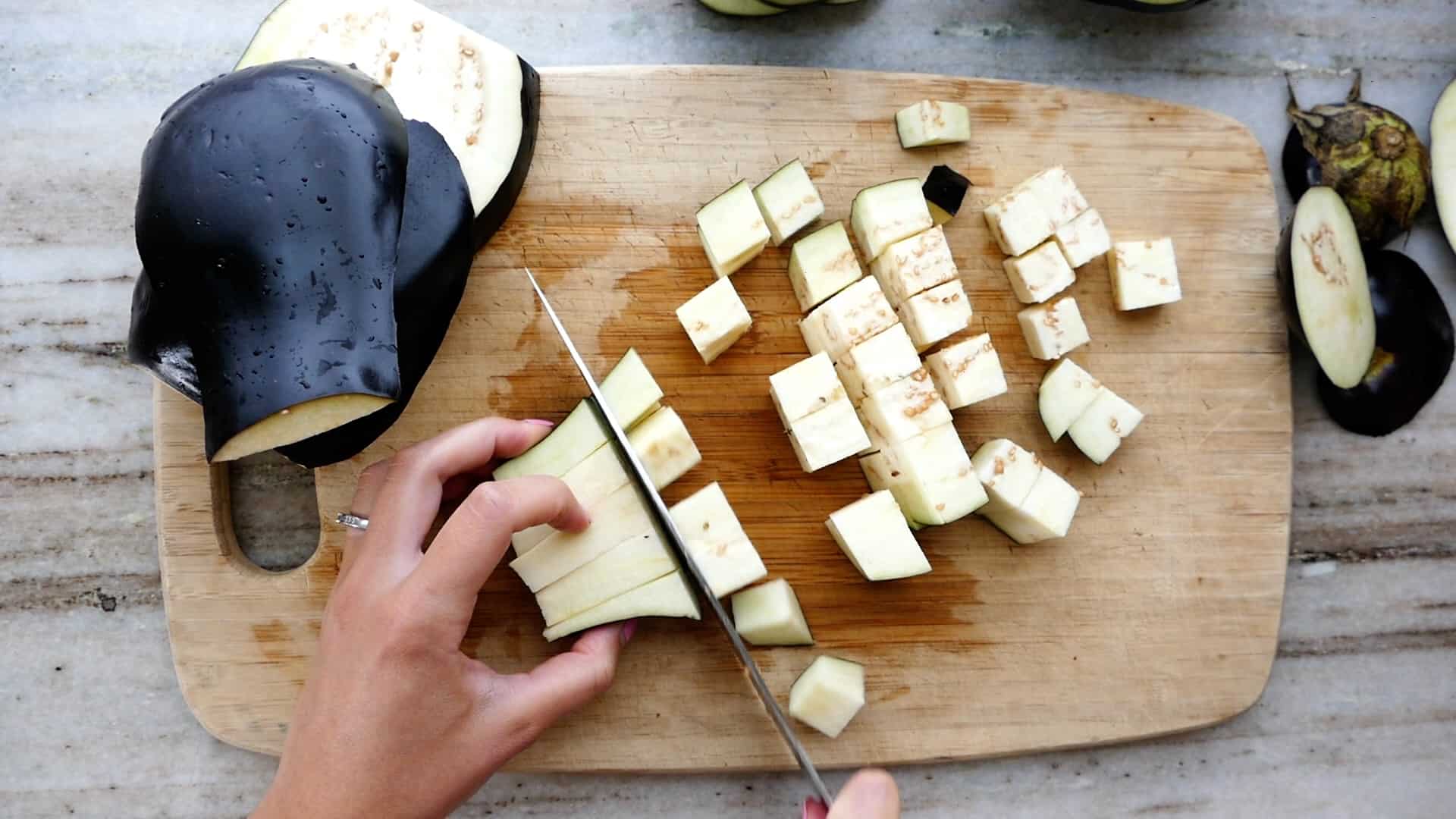 woman cutting an eggplant into cubes over a bamboo cutting board