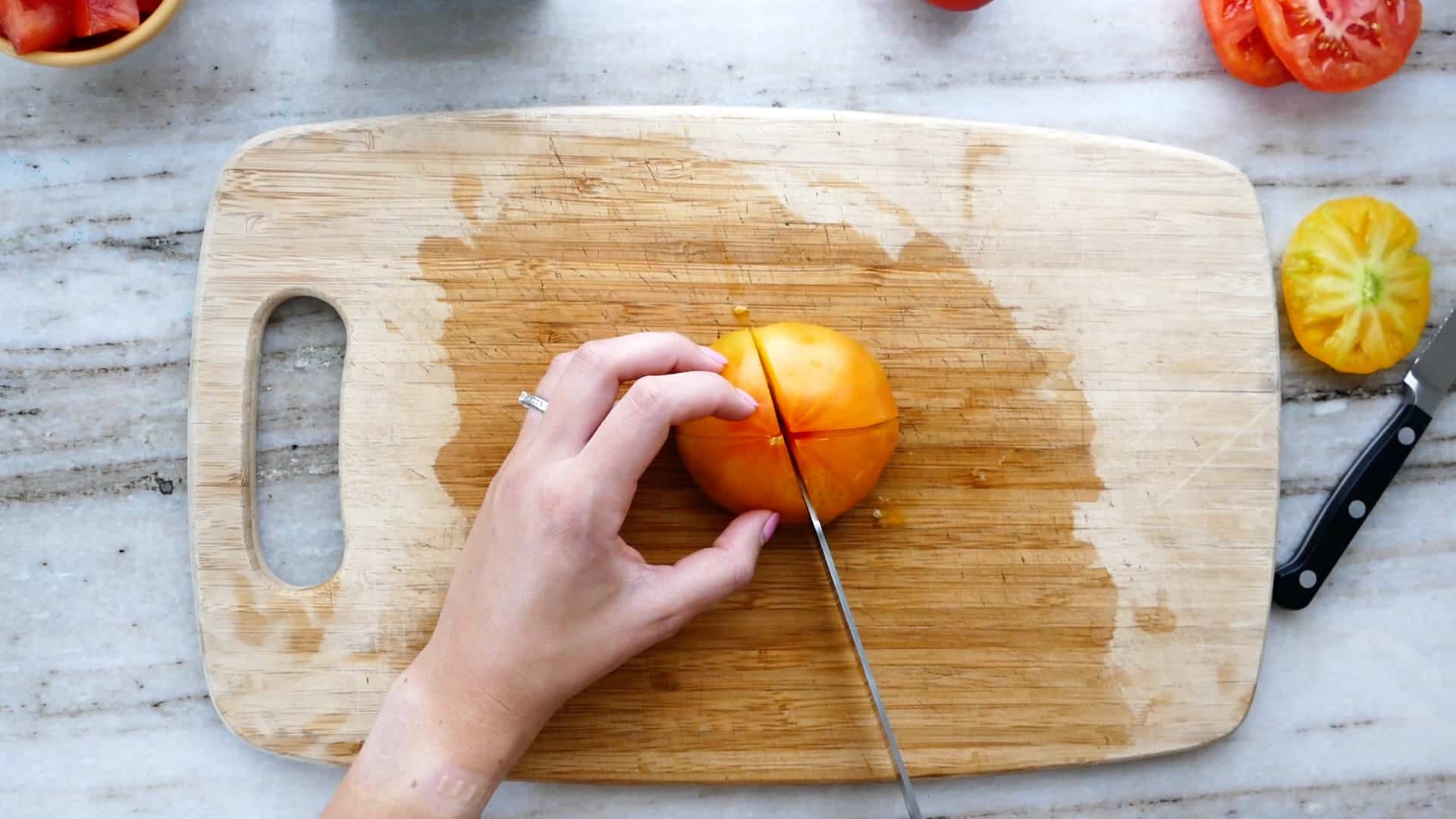 woman cutting a round tomato into quarters on a cutting board