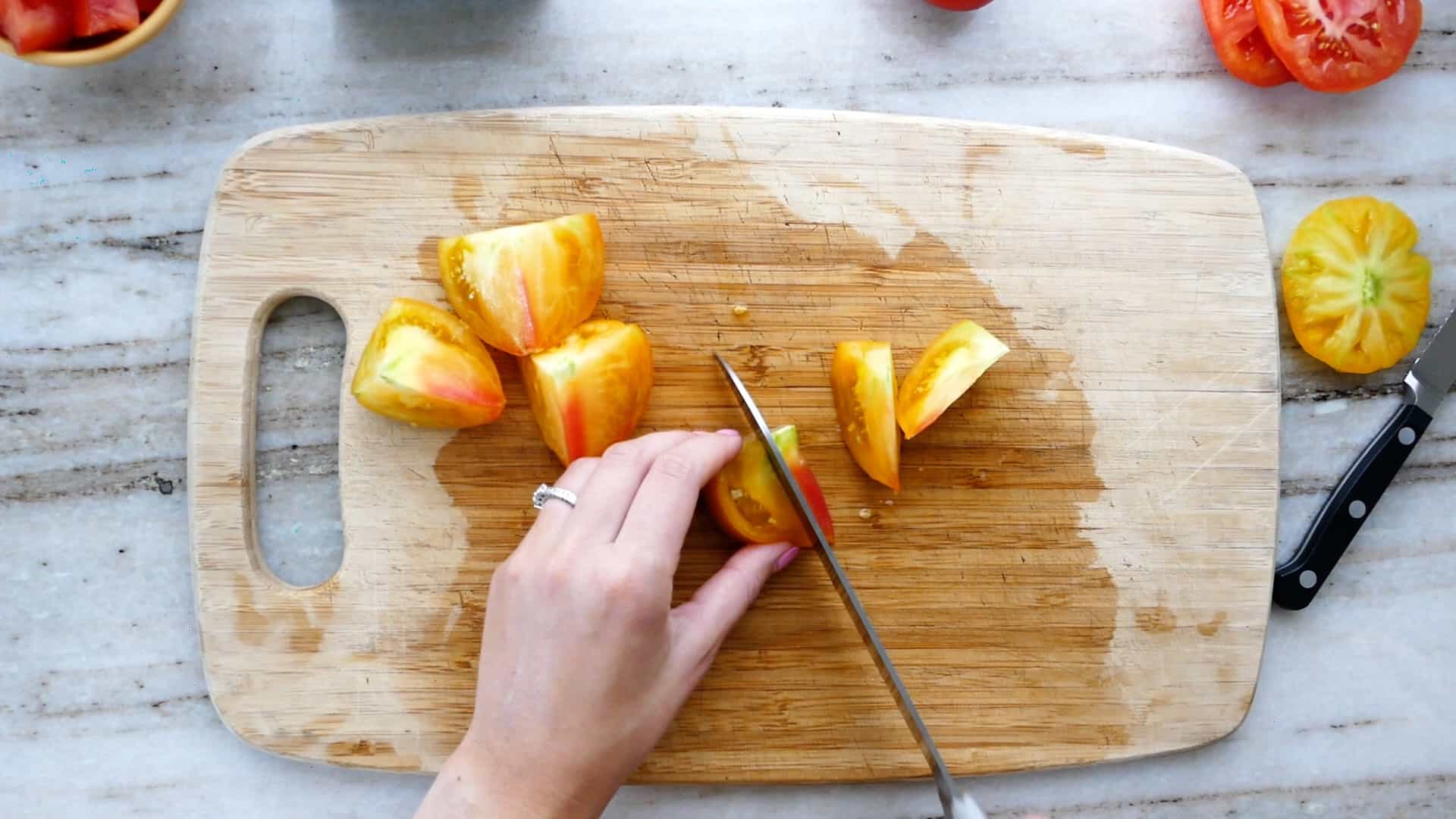 woman cutting a round tomato into wedges on a cutting board