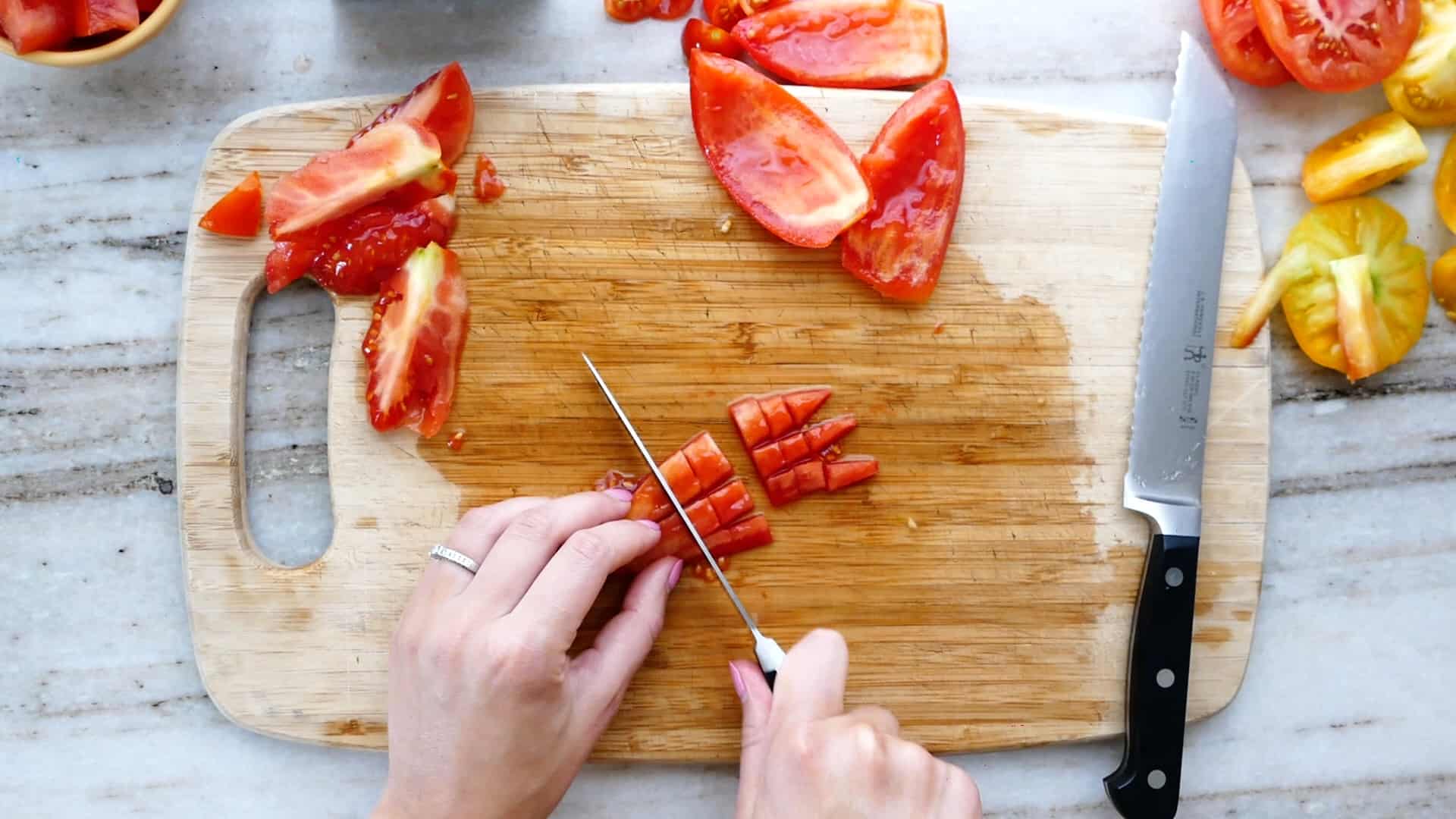 woman dicing a roma tomato with a serrated knife on a cutting board
