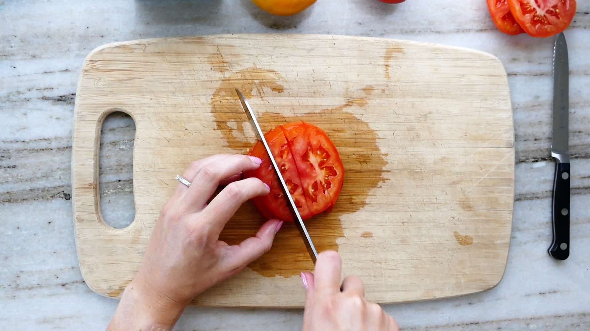 woman cutting slices of tomato into strips on a cutting board