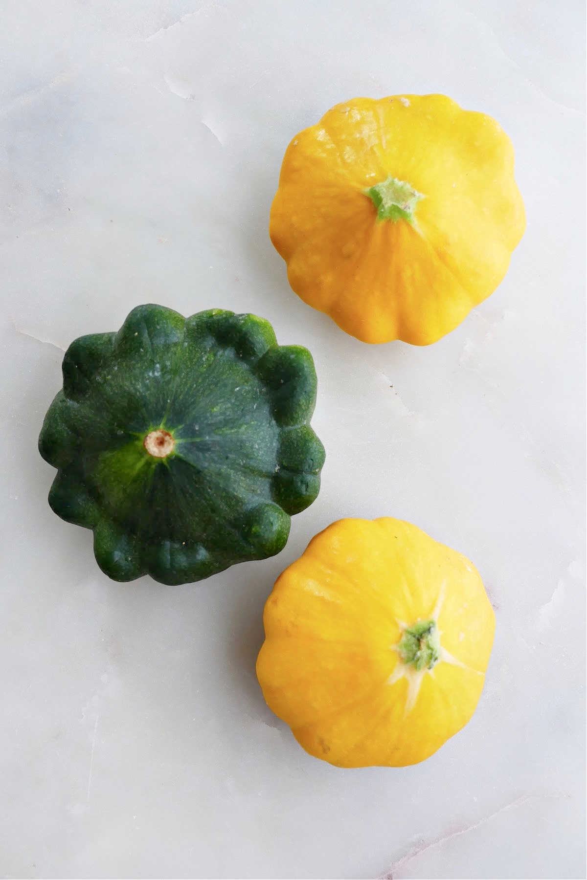 two yellow and one green patty pan squash next to each other on a counter