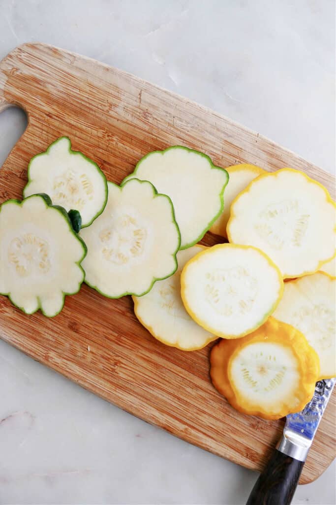 sliced patty pan squash on a bamboo cutting board next to a knife