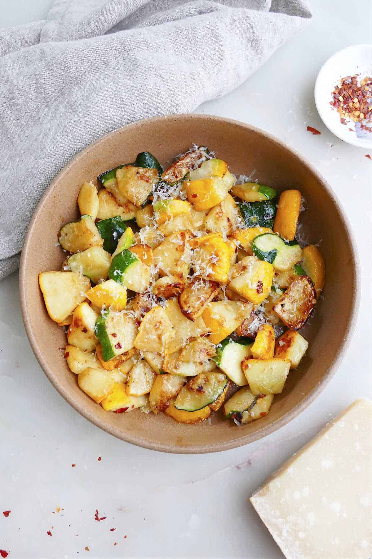 sauteed patty pan squash with parmesan cheese in a serving bowl on a counter