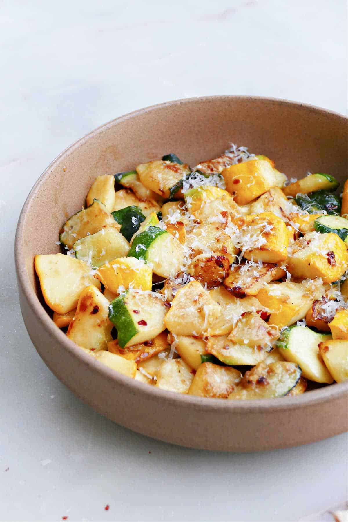 patty pan squash cooked in a skillet and topped with parmesan cheese and red pepper flakes