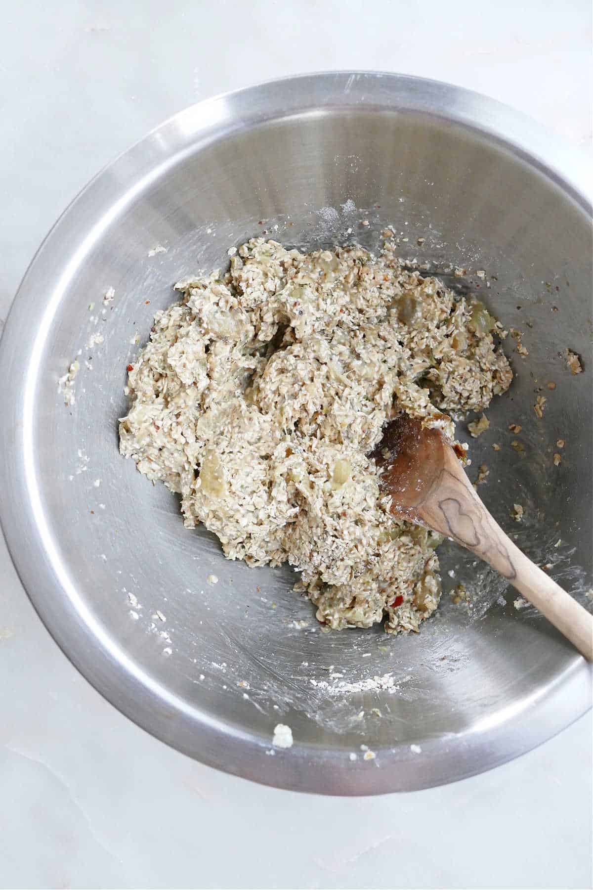 eggplant and oats being mixed together with a wooden spoon in a mixing bowl