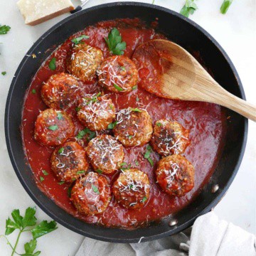 cooked eggplant meatballs in tomato sauce topped with cheese and parsley in a skillet