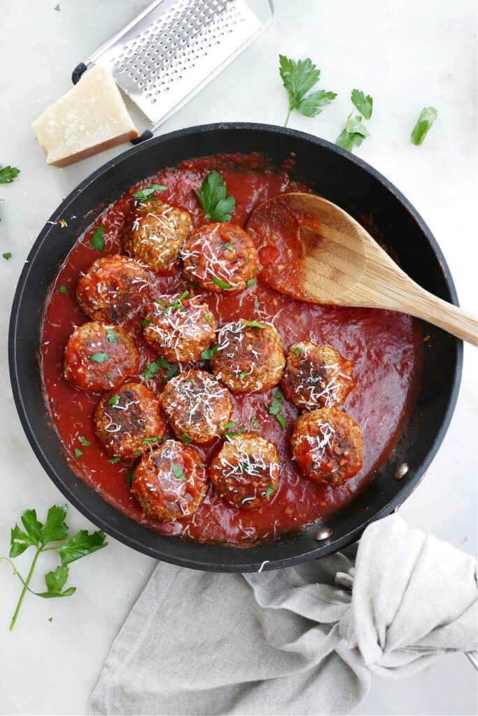 cooked eggplant meatballs in tomato sauce topped with cheese and parsley in a skillet