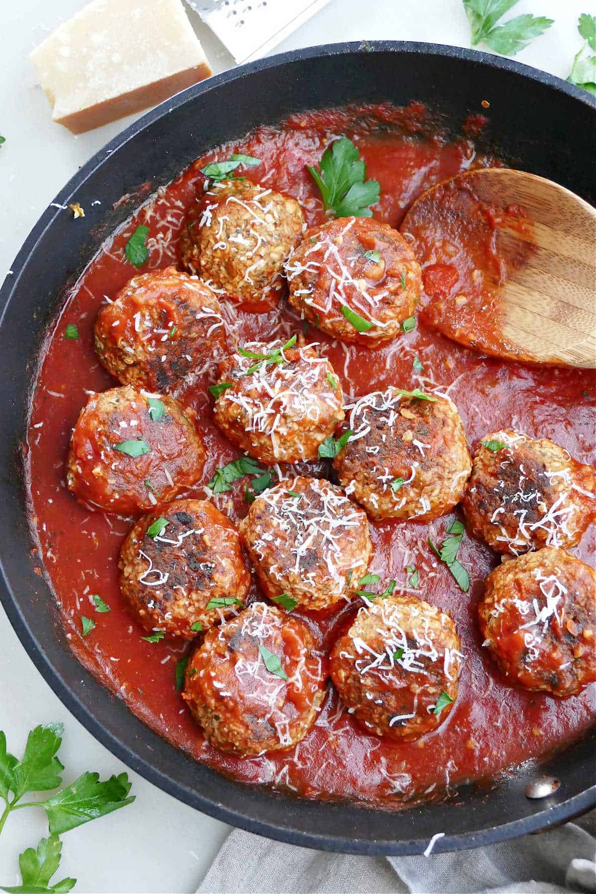 eggplant meatballs sprinkled with cheese and chopped parsley in a skillet with tomato sauce
