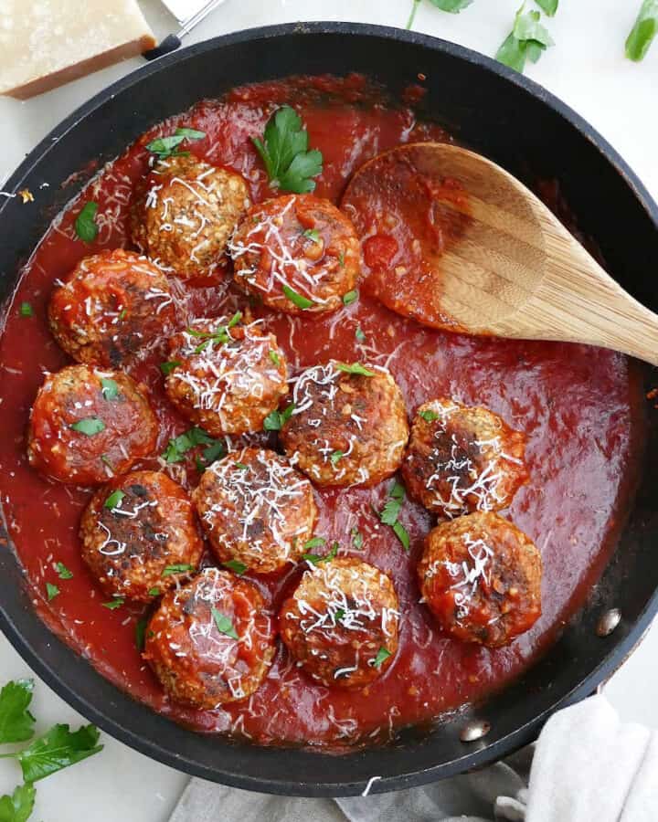 cooked eggplant meatballs in tomato sauce topped with cheese and parsley in a skillet
