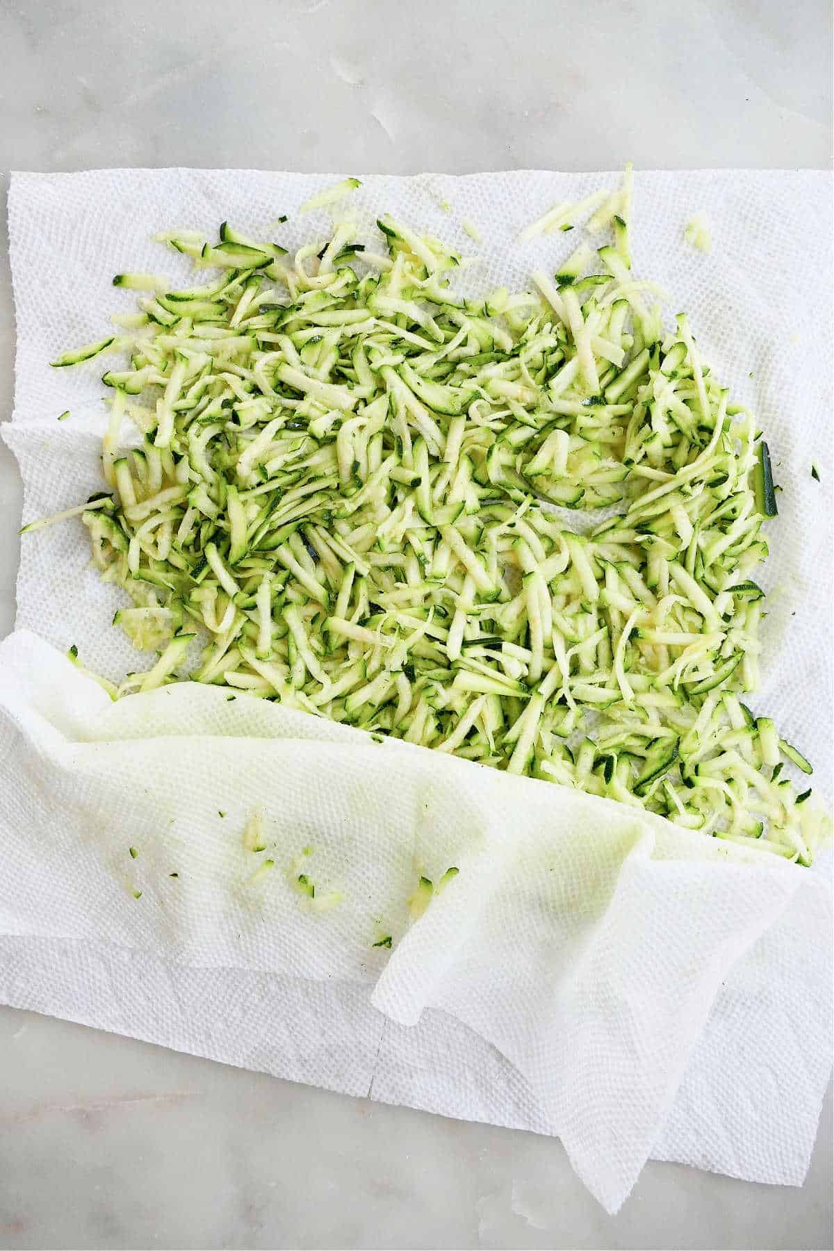 shredded zucchini being pressed in between two paper towels to remove water